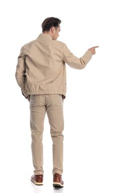 Elleri cebinde beyaz arka planda yürürken, genç ve sıradan bir adamın işaret edip yan tarafa bakması.