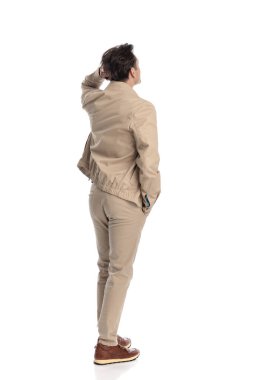 Kafası karışmış, elini cebine atarak kafasını kaşıyan, beyaz arka planda dururken kafasını kaldırıp merak eden sıradan bir adam.