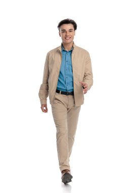 Önüne bakıp gülümseyen ve beyaz arka planda yürüyen mutlu genç adam.