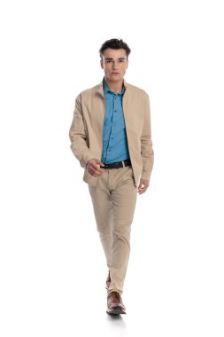 Bej ceketli kendine güvenen moda adamı ileri bakıyor ve stüdyoda beyaz arkaplanın önüne geçiyor.