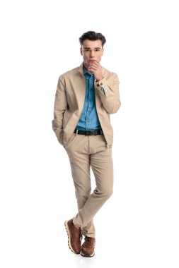 Düşünceli genç adam çene dokunuyor ve beyaz arka planda el ele dururken düşünüyor.