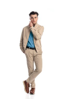 Çekici, sıradan bir adamın beyaz arka planda bir elini cebinde tutarken boynuna dokunduğu tüm vücut resmi.