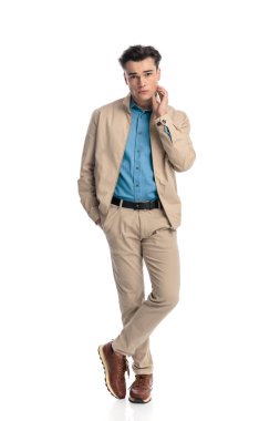 Elini cebine atarak boynuna dokunan ve beyaz arka planda dururken kendine güveni tam seksi bir erkek.