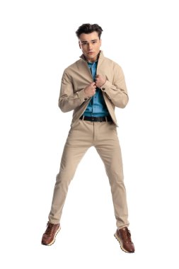 Havada zıplayıp beyaz arka planın önüne bakarken bej ceketi kapatan havalı moda adamı.