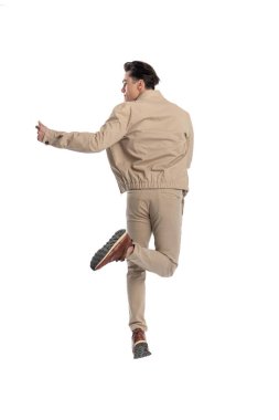 Elleri havada el kol hareketi yapan, yukarı zıplayan ve beyaz arkaplanın önüne bakan sıradan bir genç.