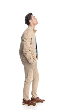 Meraklı genç adam elleri ceplerinde ve beyaz arka planda yukarı bakıyor.