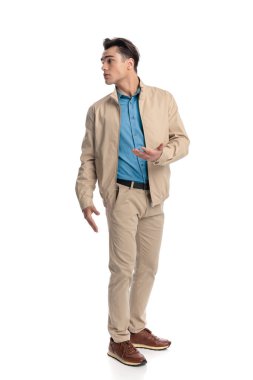 Yakışıklı genç adam beyaz arka planda dikilirken arkasına bakıyor ve açıklama istiyor.