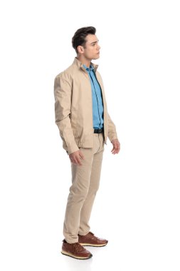 Bej ceketli sıradan bir adamın beyaz arka planın önünde durup yan gözle bakması.