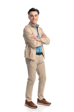 Bej ceketli, kollarını kavuşturup beyaz arka planda dururken gülümseyen mutlu sıradan bir adamın yan görüntüsü.