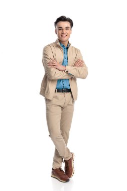 Gülümseyen sıradan bir adam kollarını kavuşturur, mutlu olur ve beyaz arka plan önünde bacak bacak bacak üstüne atarak ileriye bakar.