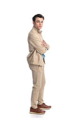 Bej ceketli, kollarını kavuşturmuş ve beyaz arka planda duran yakışıklı genç adamın yan görüntüsü.