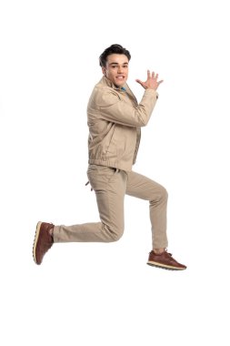 Beyaz arka planda havada zıplarken büyük ve dinamik bir şekilde poz veren bej ceketli komik sıradan adam.