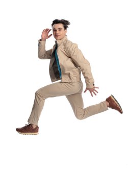 Gülümseyen ve beyaz arkaplan önünde ileriye bakan büyük ve dinamik bir hareketle havaya sıçrayan mutlu genç adamın yan görüntüsü