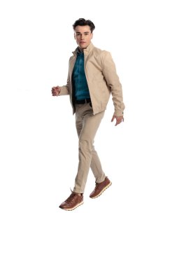 Bej ceketli sıradan bir genç öne bakıyor ve stüdyoda beyaz arkaplanın önüne geçiyor.