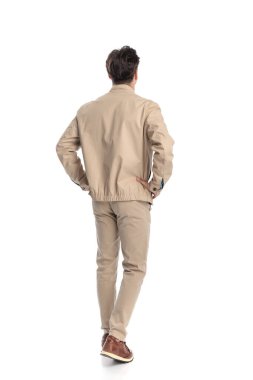 Bej renkli ceketli, spor ayakkabılı, kalçasında el ele tutuşan ve beyaz arka planda hareket eden sıradan bir moda adamı.