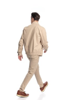 Arka planda bej ceketli genç bir moda adamı stüdyoda beyaz arkaplanın önüne atlıyor.