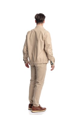 Beyaz arka planda yürüyen bej ceketli, chino pantolonlu sıradan bir adamın arka planı.