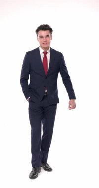 Mutlu genç iş adamı elleri ceplerinde yürüyor ve beyaz arka planda kameraya bakarken gülümsüyor.