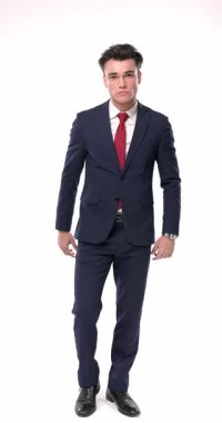 Deniz mavisi takım elbiseli seksi iş adamı kollarını kavuşturuyor, yüzlerine dokunuyor, düşünüyor, el ele tutuşuyor ve gülümsüyor, beyaz arka planda hareket ederken saç stilini ayarlıyor.