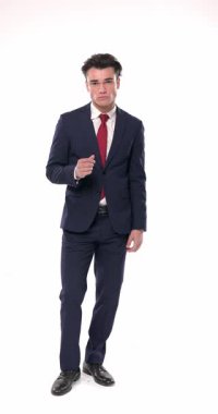 Lacivert takım elbiseli çekici genç işadamı elini cebine sokup beyaz arka planda gülümsemeden önce hareket ediyor ve poz veriyor.