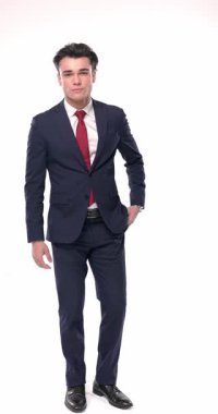 Lacivert takımlı zengin genç adam parmaklarını ovuşturuyor ve para işareti yapıyor, ceplerinde el ele tutuşuyor ve beyaz arka planda yer arıyor.