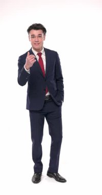 Lacivert takım elbiseli mutlu genç işadamı elini kullanarak bir davetiye yapıyor, gülümsüyor ve el ele tutuşup beyaz arkaplanda el ele tutuşmadan önce misafirperverlik gösteriyor.