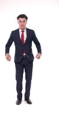 Lacivert takımlı yakışıklı, zarif bir adam gülümserken beyaz arka planda el hareketi işareti yapıyor.