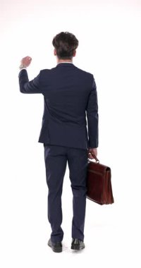 Bavulu kaşınan, kafa karıştıran, el ele tutuşan ve beyaz arka planda duran lacivert takım elbiseli, kafası karışık genç bir adam.