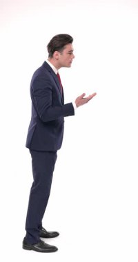 Lacivert takım elbiseli zarif genç işadamının yan görüntüsü sırada bekliyor, konuşuyor, elleriyle el hareketi yapıyor ve ellerini cebine koymadan önce başını sallıyor.