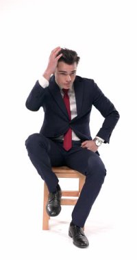 Yakışıklı genç iş adamının saç stilini düzenleyen, aynaya bakan, sandalyeye oturup beyaz arka planda gülümseyen ve kravatı düzelten dikey videosu.