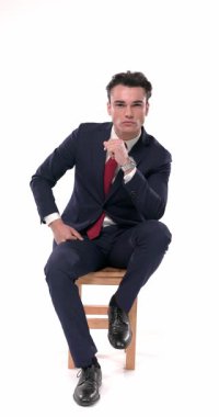 Ciddi genç iş adamları dizlerinin üstünde, çeneye dokunuyor, ileriye bakıyor ve beyaz arka plan üzerinde düşünüyor.