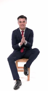 Mavi takımlı mutlu bir gencin tahta sandalyede otururken el çırptığı, başparmak hareketi yaptığı ve gururlandığı dikey bir video.