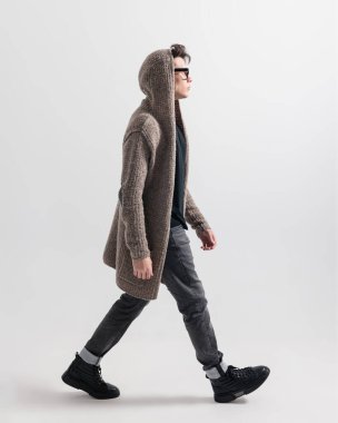 Kapüşonlu sıradan bir genç adamın gri arka planda yürürken ve yan tarafa bakarken yan görünümü