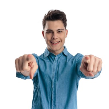 Mavi gömlekli yakışıklı genç adam, beyaz arka planda parmaklarını öne uzatıp gülümsüyor.