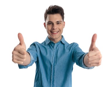 Mavi kot gömlekli mutlu genç adam beyaz arka planda başparmak hareketi yapıyor ve gülümsüyor.