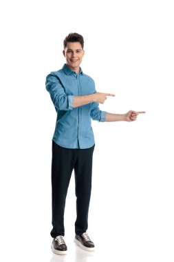 Kot gömlekli seksi genç adam parmaklarını yana doğru gösteriyor ve gülümsüyor beyaz arka plan önünde sunuyor ve duruyor.