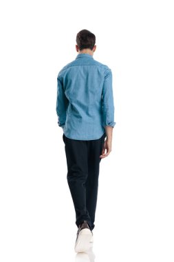 Beyaz arka planda mavi kot gömlekli sıradan bir genç adam yürüyor.