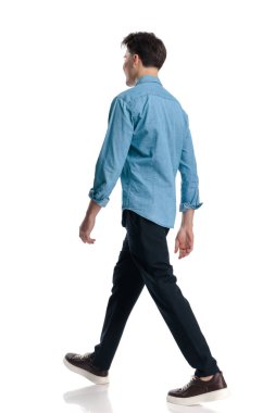 Stüdyoda beyaz arka planda yürüyen ve gülümseyen sıradan genç bir adamın yan görüntüsü