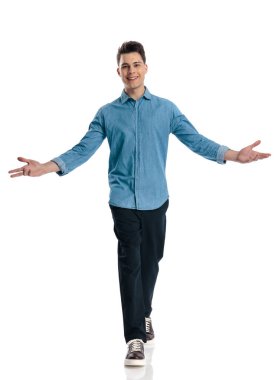 Mavi kotlu tişörtlü yakışıklı adam gülümsüyor, kollarını açıyor ve beyaz arka planda yürüyor.