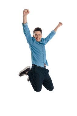 Kafasının üstünde yumrukları olan neşeli genç bir adam havaya zıplıyor ve zaferi beyaz arka planda kutluyor.