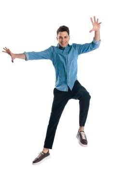 mavi kot gömlekli dinamik bir adam havada zıplıyor ve beyaz arka planda heyecanlanıyor.