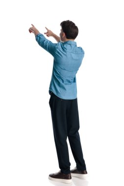 Mavi kot gömlekli sıradan bir genç adam, beyaz arka planda dikilip, parmaklarını işaret ediyor.