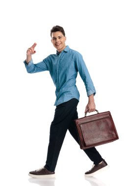 Yakışıklı, asker selamlayan, gülümseyen ve beyaz arka planda bavulla yürüyen genç bir adam.