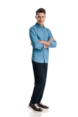 Mavi kot gömlekli kendine güvenen genç adam kollarını kavuşturuyor ve beyaz arka planda gülümsüyor.