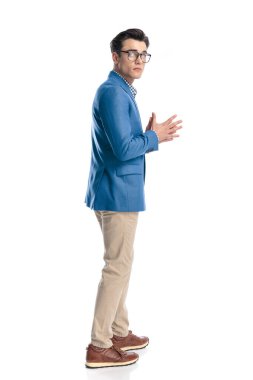 Mavi ceketli, beyaz arka planda yürürken avuçlarını ovuşturan sıradan bir gencin yan görüntüsü.