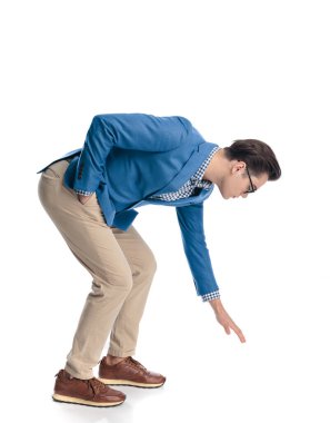 Gözlüklü genç adam beyaz arka planda dururken öne eğilip yerden bir şey alıyor.