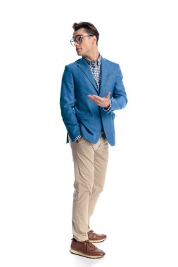 Cebinde gözlüğü olan yakışıklı genç adam, omzunun arkasına bakıyor ve beyaz arka planda sırada beklerken anlatıyor.