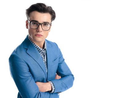 Gözlüklü, kollarını kavuşturan ve beyaz arka planda kendinden emin bir şekilde ileriye bakan seksi genç adam.