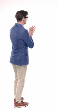 Mavi ceketli genç adamın yan görünüşü. Gözlerini kaçırıyor, el çırpıyor, kameraya dönüyor ve beyaz arka planda baş parmak hareketi yapıyor.