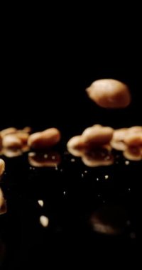 Siyah bir masaya düşen fıstıklı şelale koyu siyah arka planda parlıyor, lezzetli atıştırmalıklar ve besin maddeleriyle dolu.